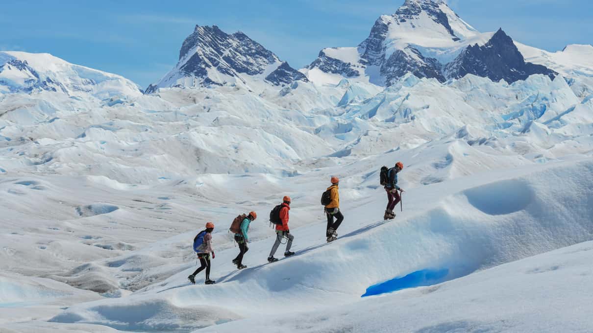 A line of hikers crossing the white surface of Perito Moreno Glacier on the Big Ice trek, snowy peaks behind