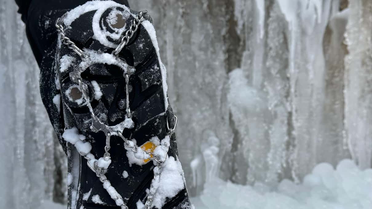 A frozen waterfall of white and blue icicles hanging down a golden and grey limestone wall