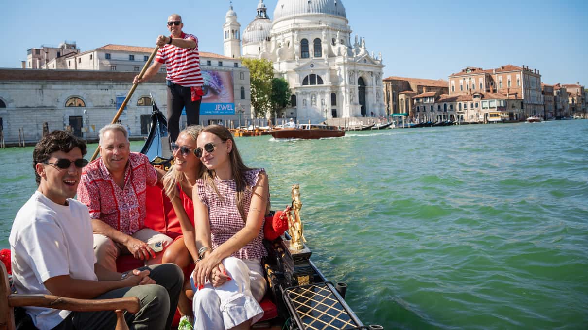 Rodzina w gondoli na Canal Grande, za nią gondolier w koszulce w paski, w tle kopuła bazyliki Santa Maria della Salute