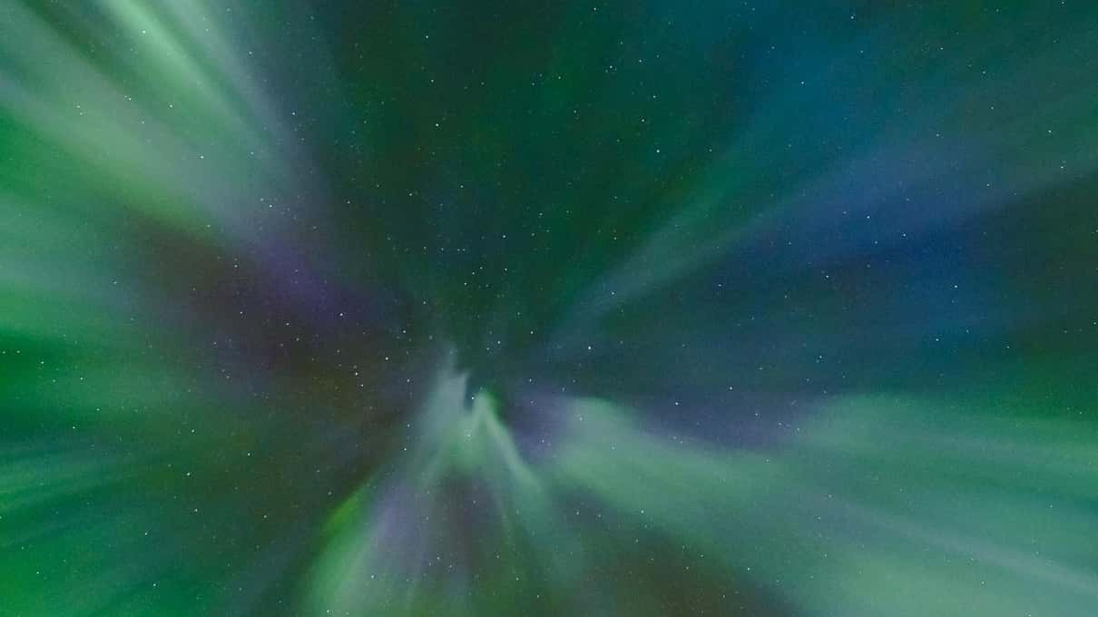A green and violet aurora spiralling overhead in a corona, seen straight up from the ground