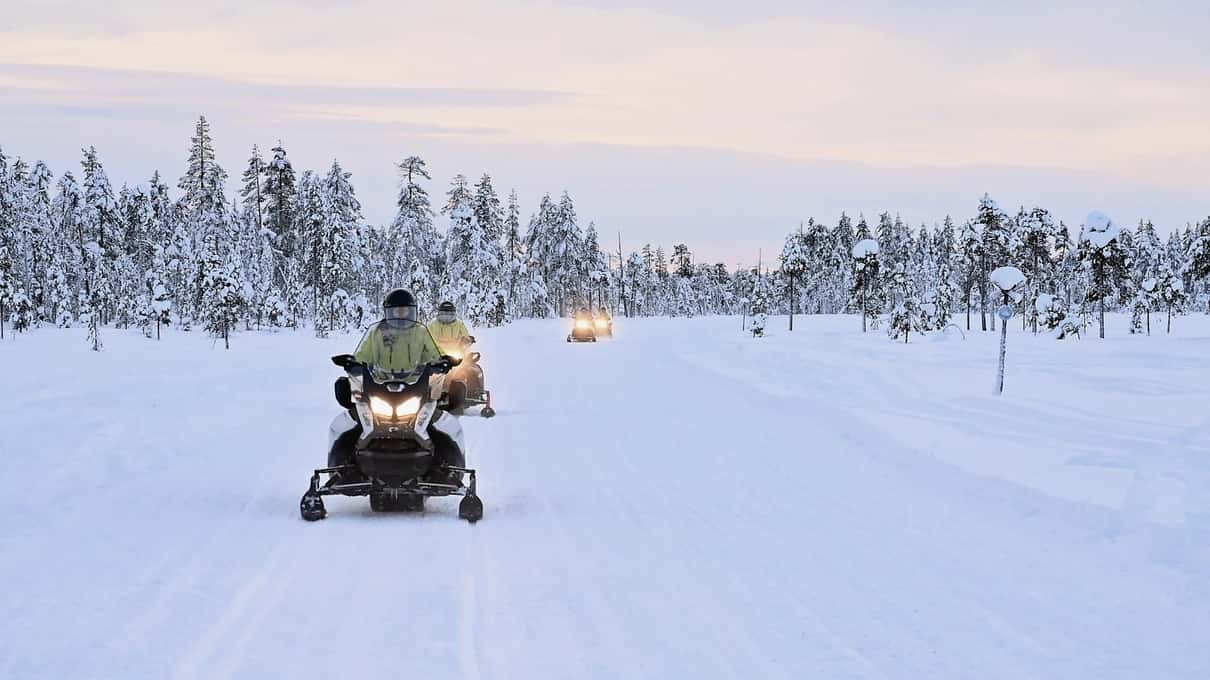 A line of snowmobiles following a trail near Levi under a pink low winter sun