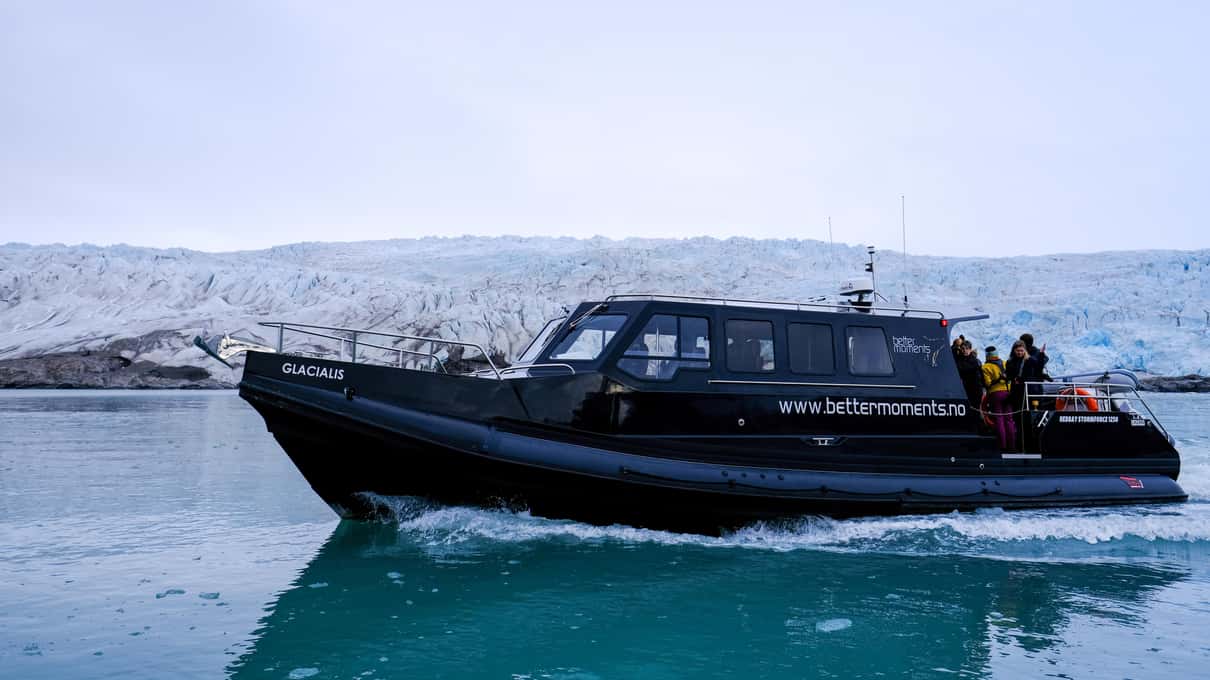 Skua Nature's dark covered boat cutting through green water past a snowy shore