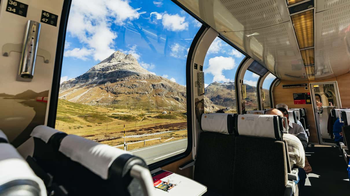 Snowy mountains seen through the large curved window of a panoramic Bernina Express car