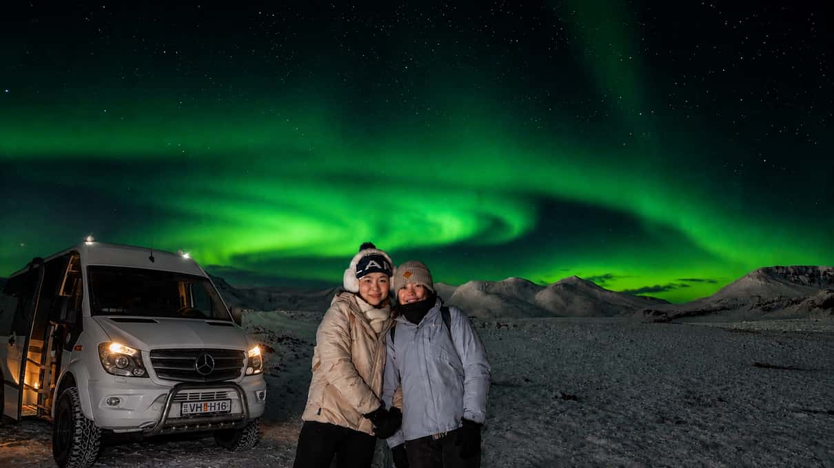 Weißer Geländewagen-Minibus mit eingeschalteten Scheinwerfern unter grünem Polarlicht in Island
