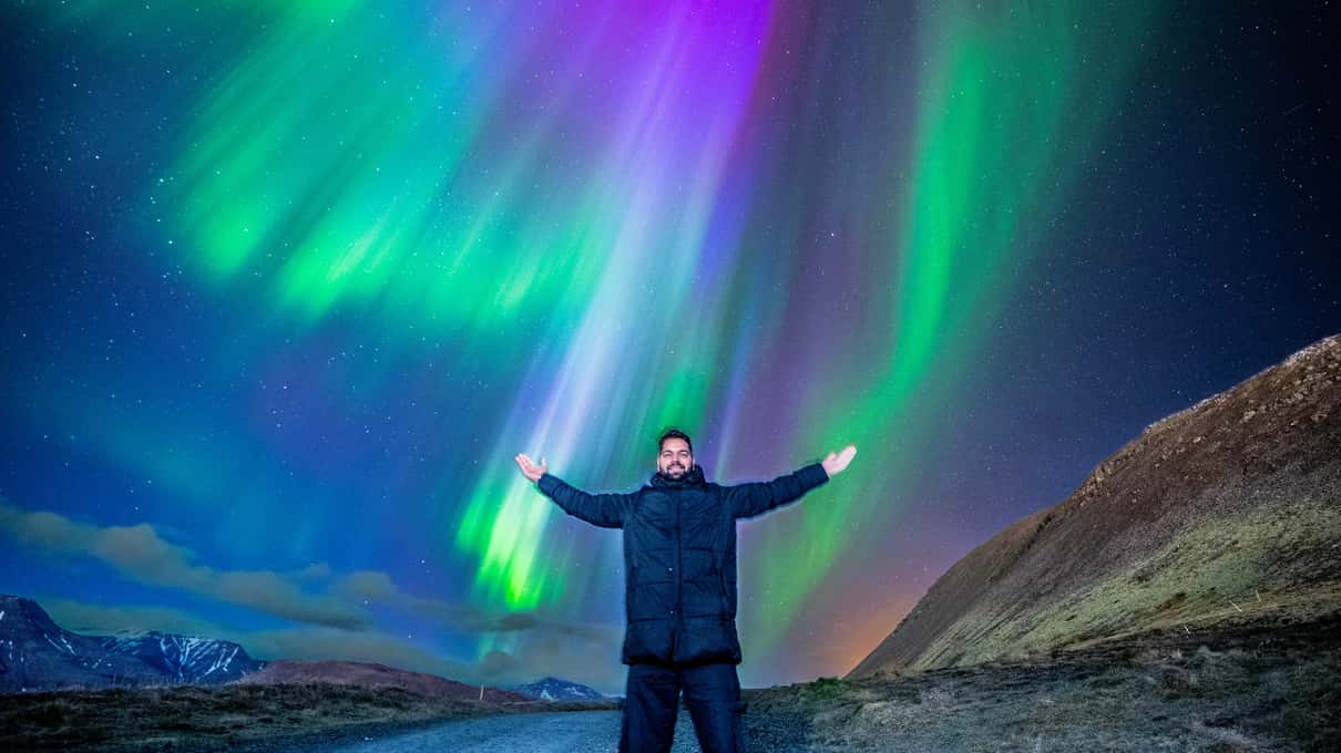 Viajero con los brazos abiertos bajo una aurora boreal magenta y verde en Islandia