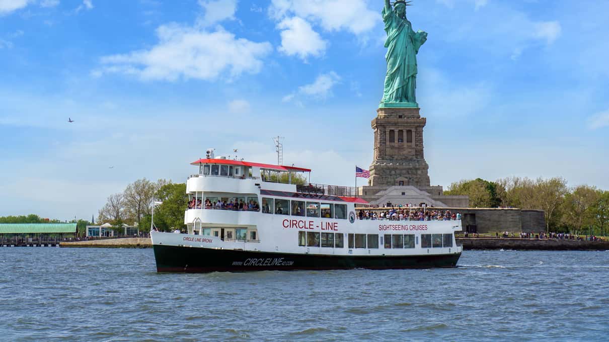 Circle Line sightseeing boat passing in front of the statue on a clear spring day