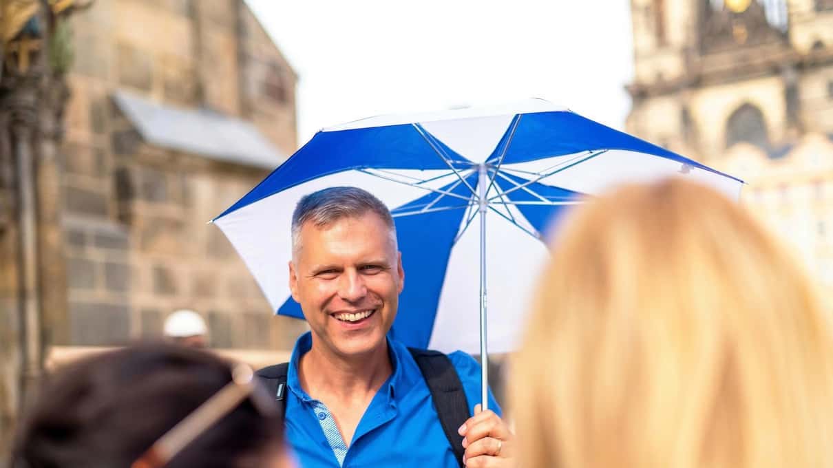 A Get Prague Guide walking tour guide raising a blue and white umbrella so the group can follow
