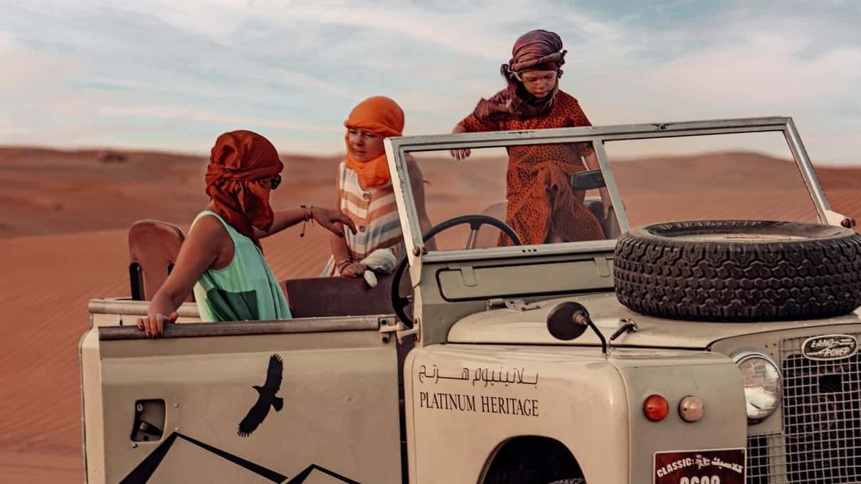 Ospiti a bordo di una Land Rover d’epoca color crema, scoperta, tra le dune rosse