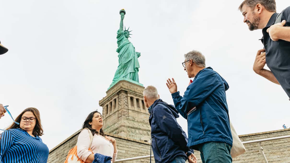 Guide raising his hand to explain the statue to a small group at the foot of the pedestal