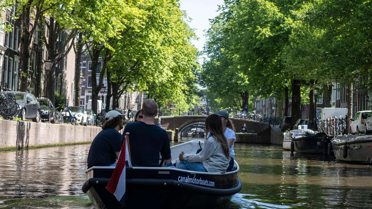 Kleine Gruppe steuert selbst ein offenes Mietboot über eine von Bäumen gesäumte Gracht
