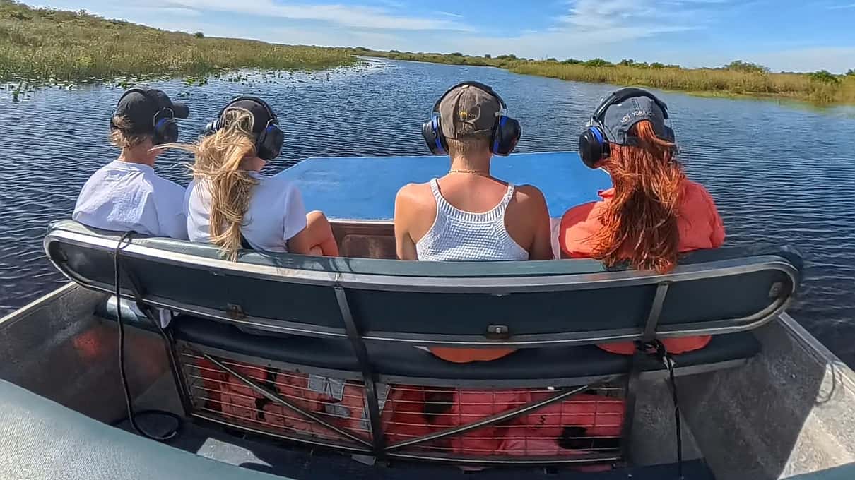 Riders in noise-reducing headphones on the bench of a small Tours by Max airboat crossing open water
