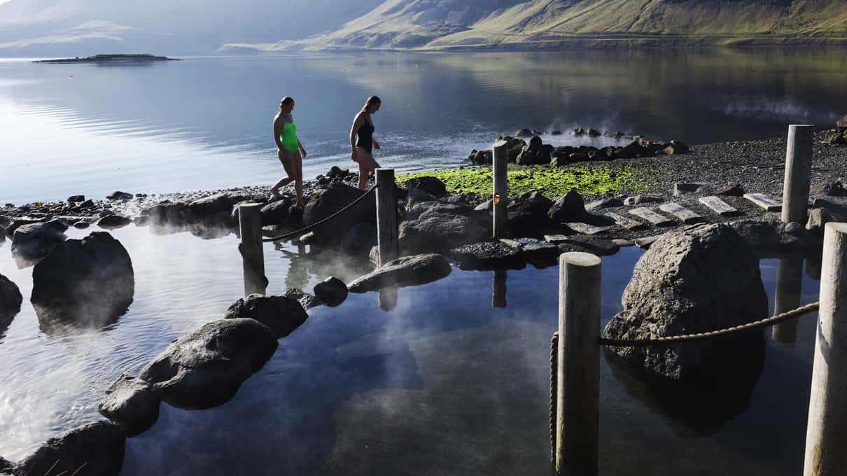 A wooden walkway leading between steaming geothermal pools at Hvammsvik Hot Springs