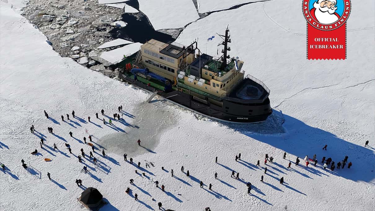 Aerial view of the icebreaker Arktis in its broken channel with a crowd of guests out on the sea ice