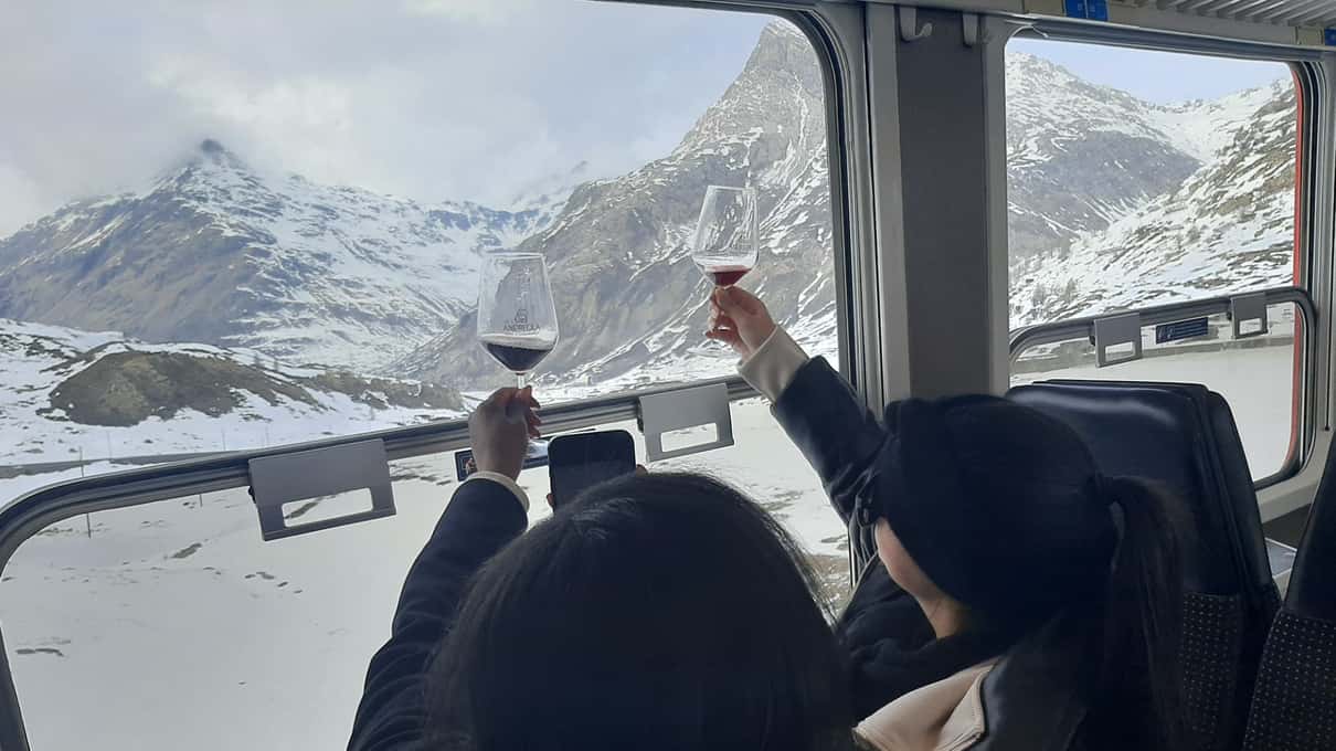 Travelers raising glasses of wine in the train carriage with snowy peaks outside the window