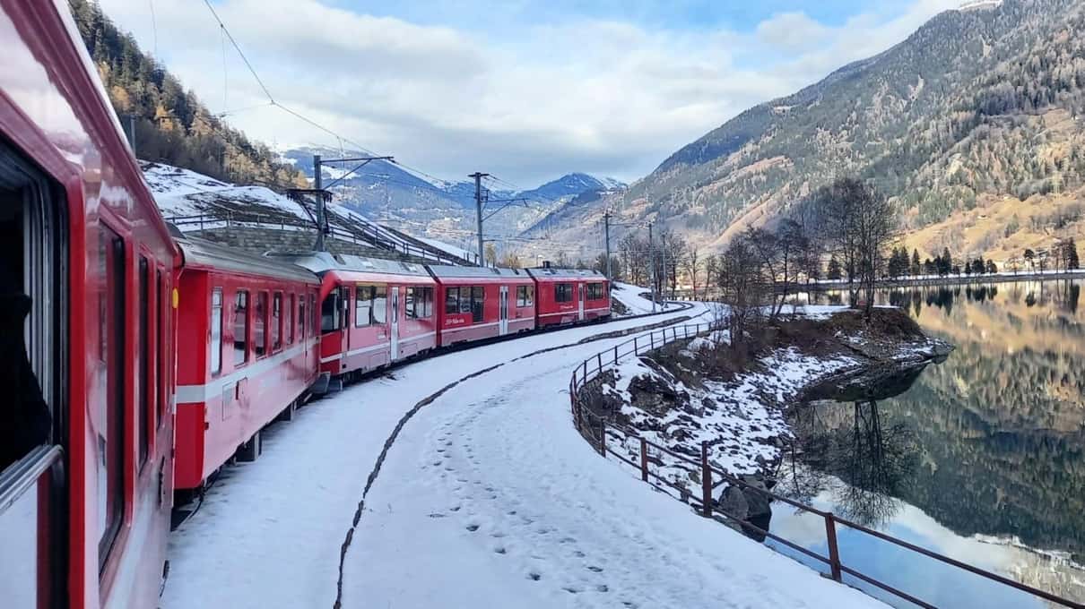 The red Bernina train running through deep snow piled up beside the track