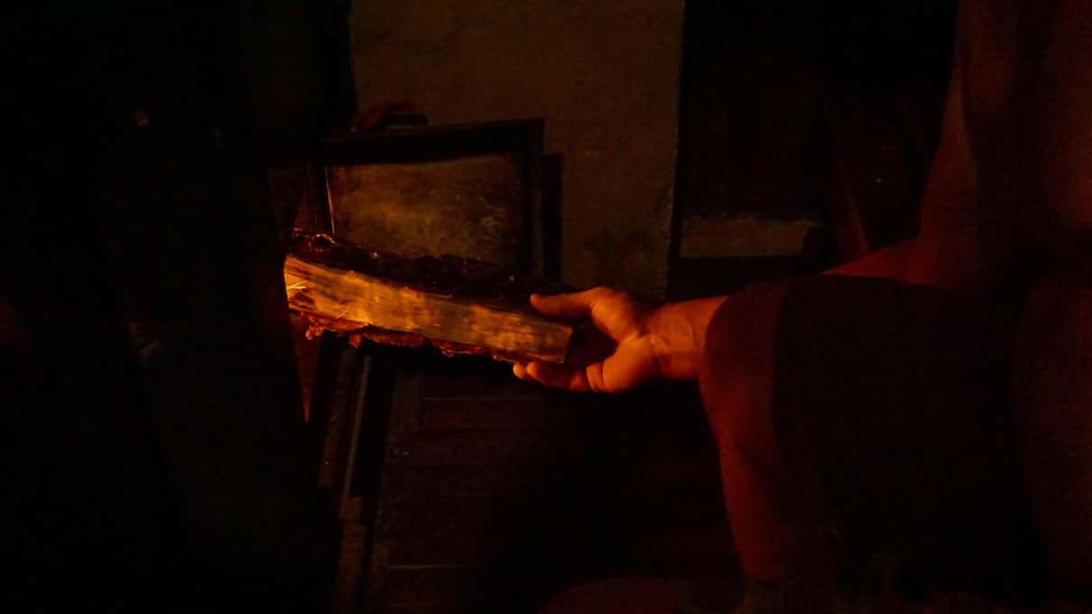 A hand feeding a split birch log into the glowing firebox of a sauna stove