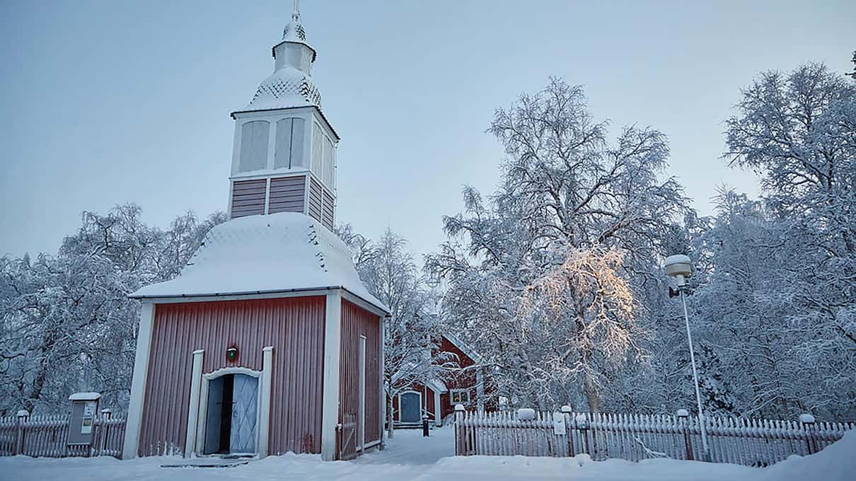The red wooden church of Jukkasjärvi under snow with frosted birch trees around it