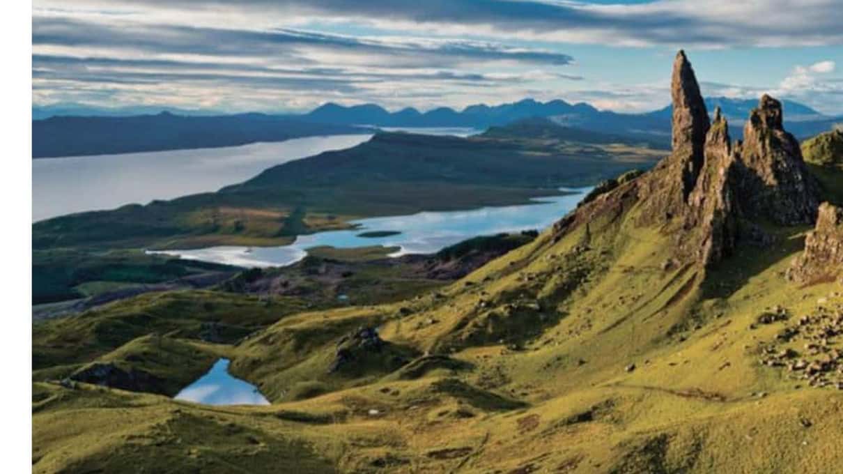 The Old Man of Storr pinnacle rising above green terraces with the Sound of Raasay and mainland hills beyond