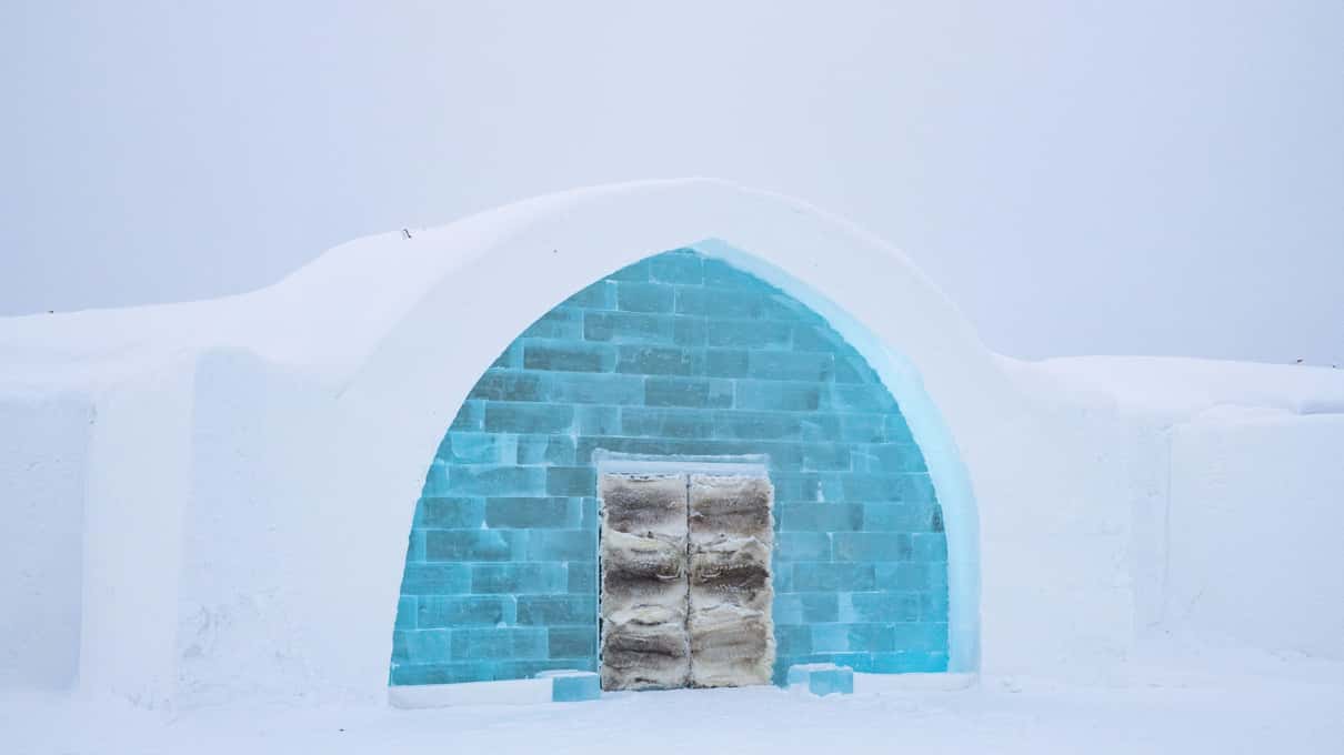 A doorway of turquoise ice blocks with reindeer-hide doors set into a snow wall