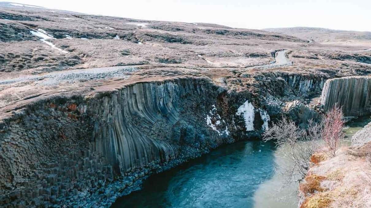 The canyon seen from above, its column walls dropping to a blue river with patches of snow on the rim