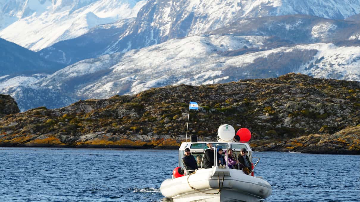 A small boat with passengers in red jackets on the Beagle Channel below snowy mountains