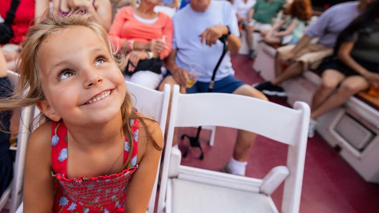 A smiling young girl on the deck of a Chicago river cruise boat looking up at the tall buildings