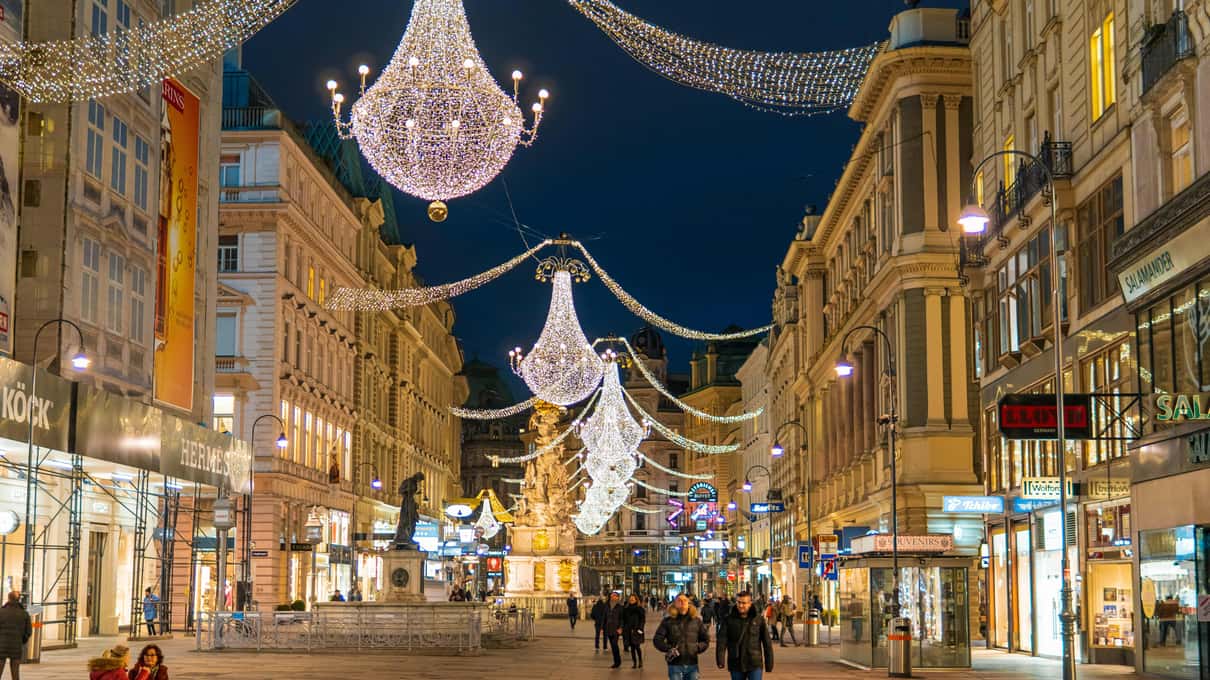 Giant chandeliers of white lights hanging over the Graben at night, with shoppers walking below