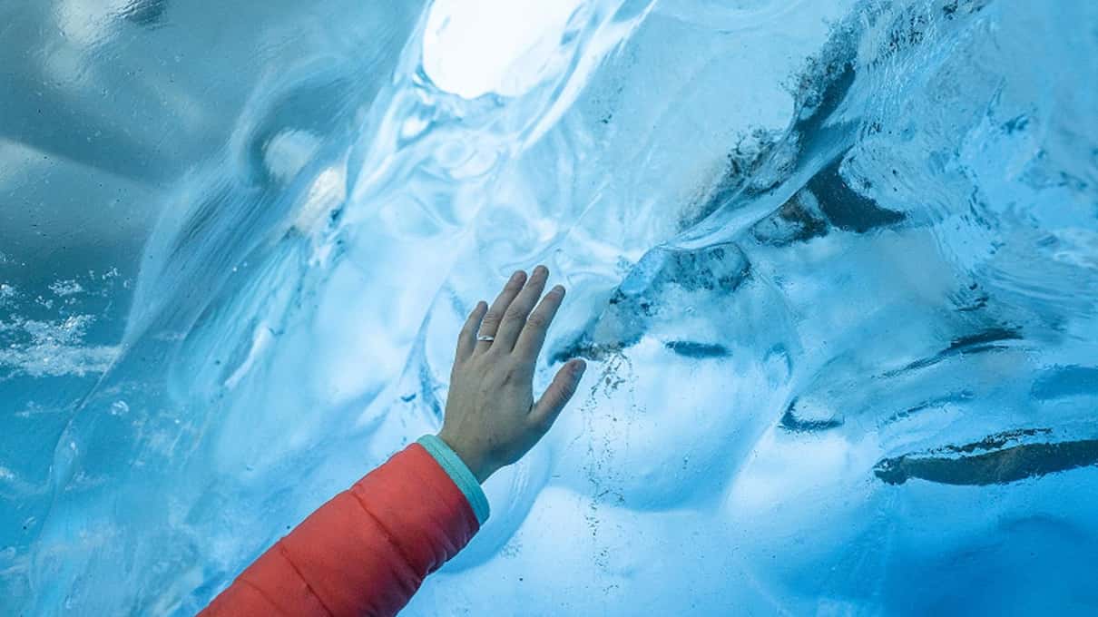 A visitor's hand pressed against the deep blue ice of the Perito Moreno Glacier wall