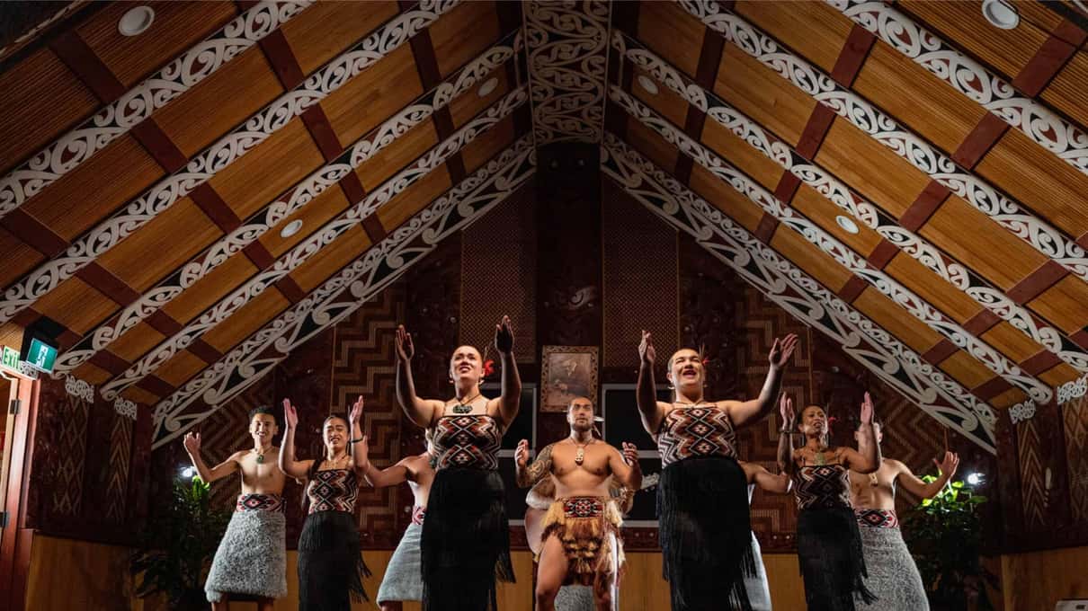 Performers in traditional dress singing inside the carved meeting house at Te Puia