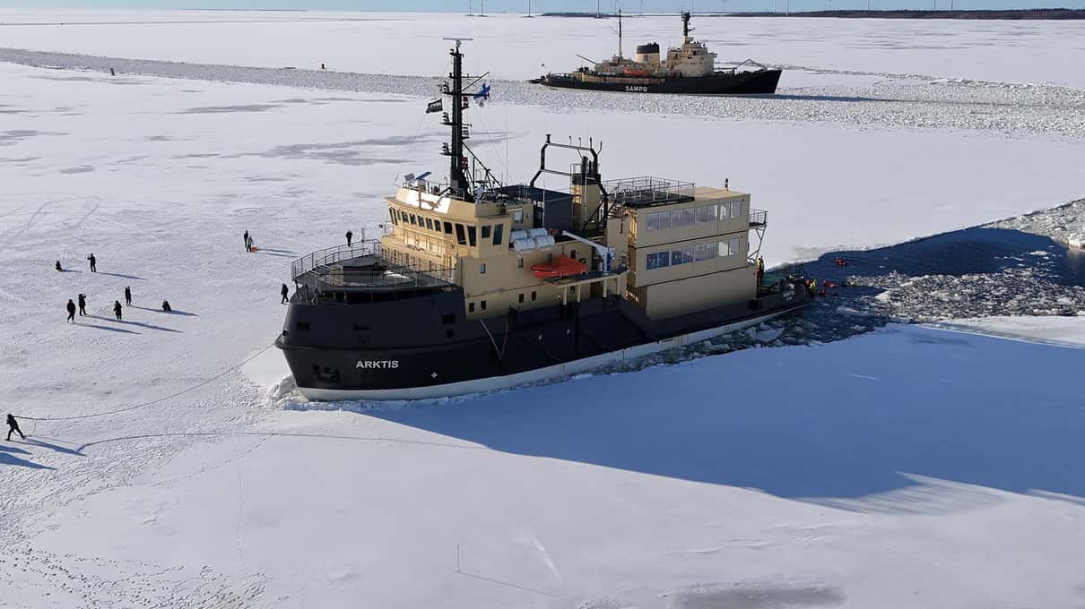 Icebreaker Arktis with a cream superstructure stopped in sea ice while guests walk around it