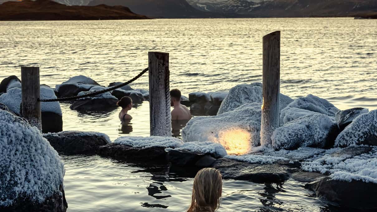 Steaming pools and wooden posts on the Hvammsvik shore at sunset over the fjord