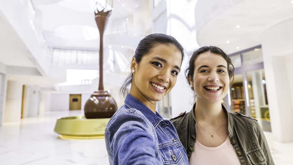Two smiling visitors in front of the giant chocolate fountain at the Lindt Home of Chocolate