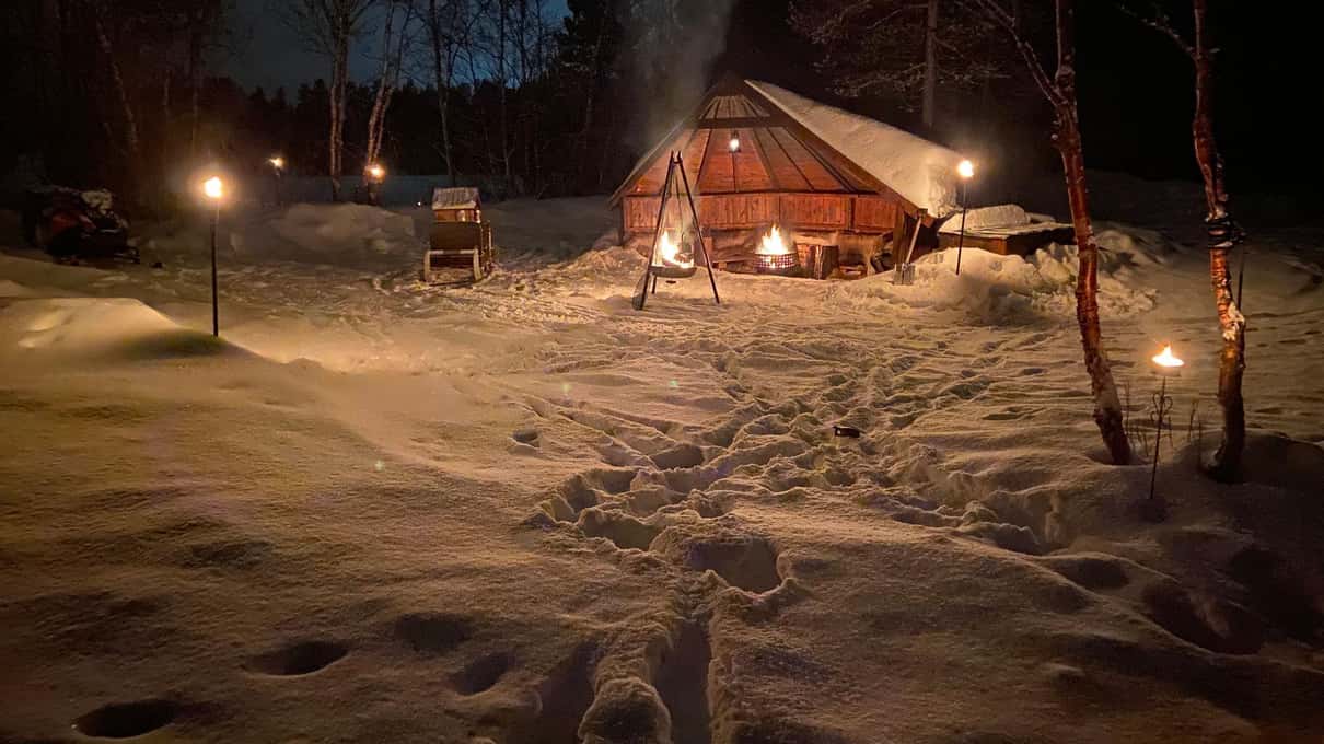 A lit wooden cabin among snow-covered trees on a dark cloudy night with no aurora in the sky