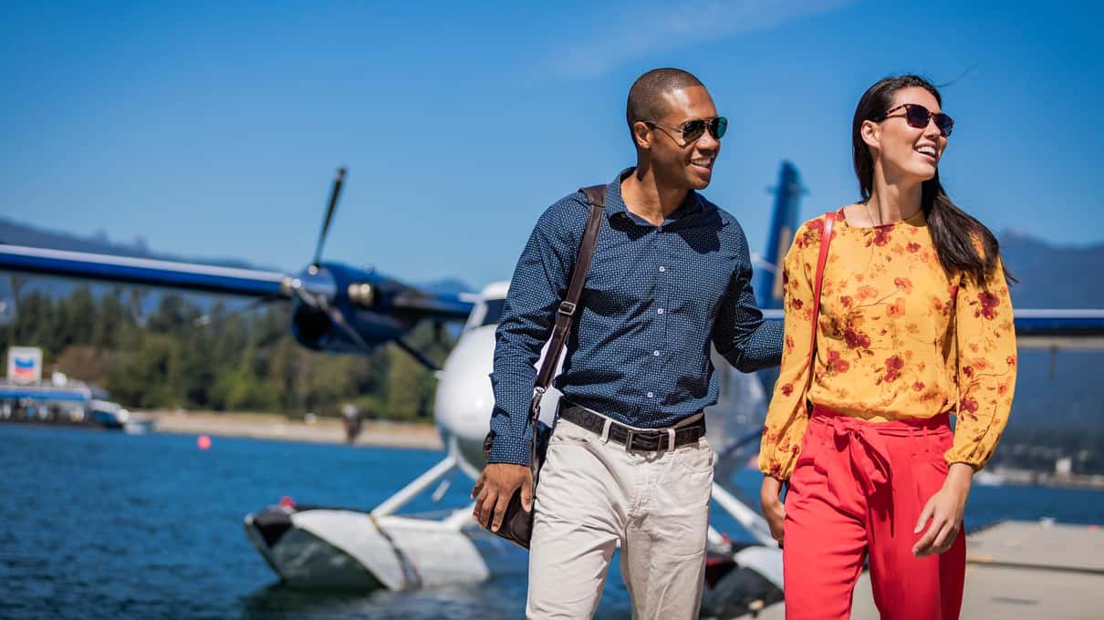 A couple in sunglasses walking along the floating dock away from a parked floatplane after landing