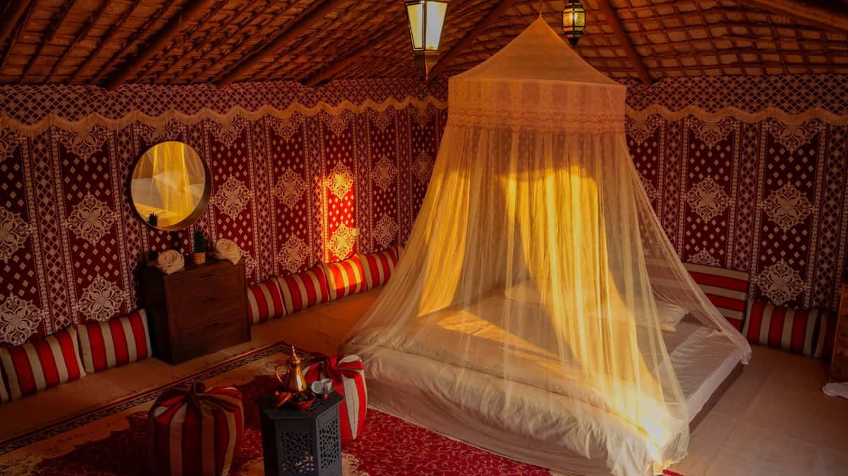Interno di una tenda beduina decorata, con un letto chiuso da una zanzariera illuminata dalle lanterne