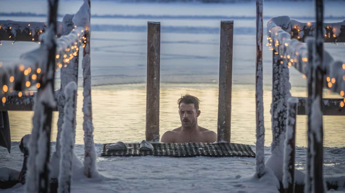 A bather standing in an ice hole between birch trees on a frozen lake