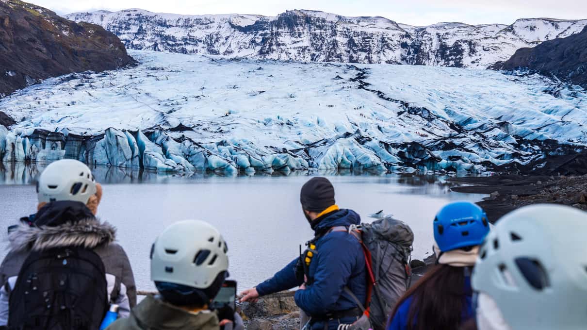 A group in climbing helmets standing above the glacier lagoon at the foot of Sólheimajökull
