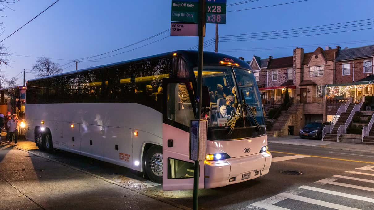 Big white tour coach parked on a quiet residential Brooklyn street at dusk