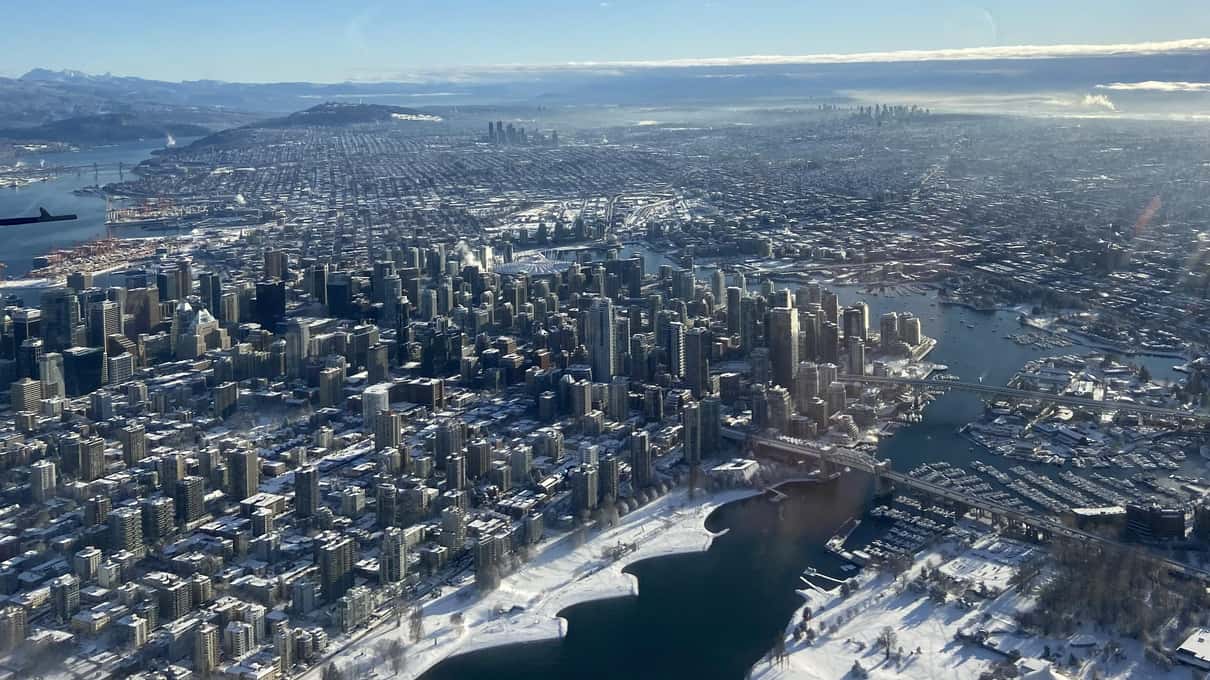 Downtown Vancouver and the harbor seen from a floatplane in winter, with snow lying on the rooftops and the hills