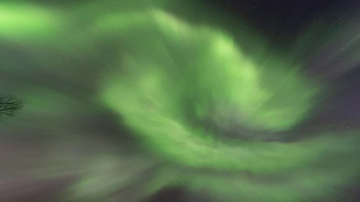 A wide swirl of green aurora filling the whole night sky above dark ground in Finnmark