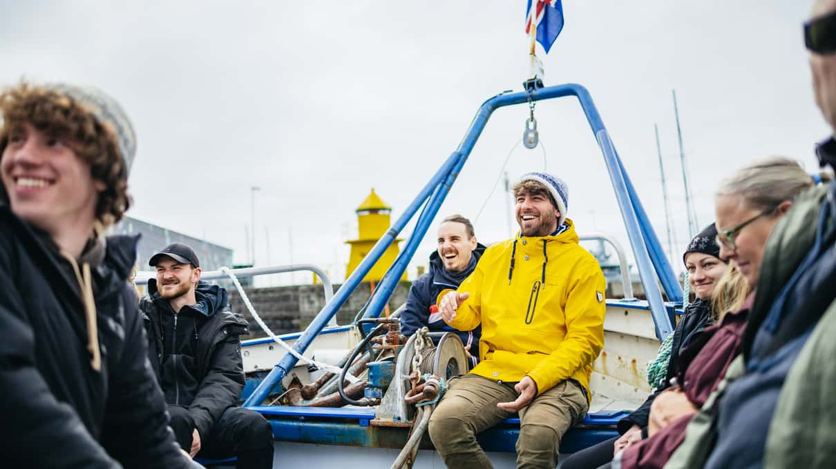 Passengers in yellow and blue jackets on the open deck of a small boat beneath an Icelandic flag