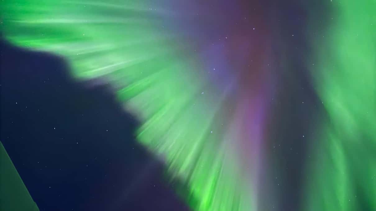 A burst of violet and green aurora rays fanning out across a deep blue night sky