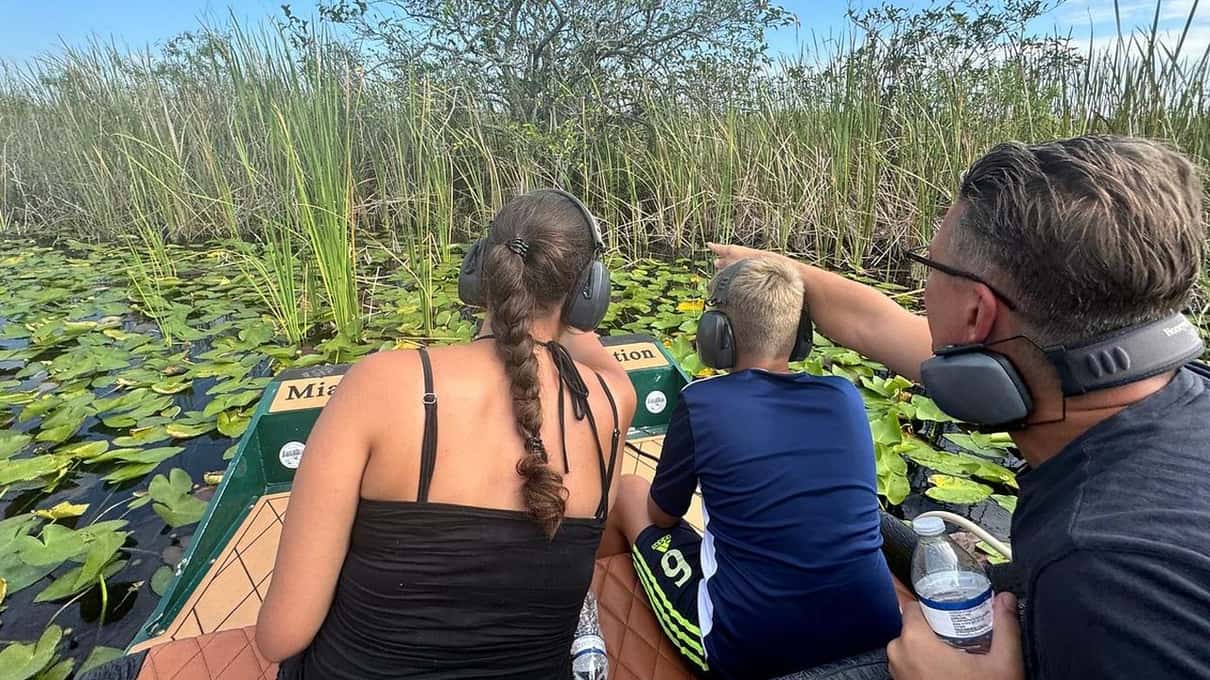 Family on a small green airboat among lily pads with the captain wearing ear protection