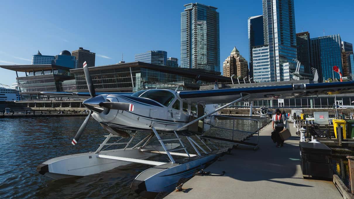A Seair Seaplanes Beaver floatplane moored at the downtown Vancouver dock with the Vancouver Convention Centre and towers behind