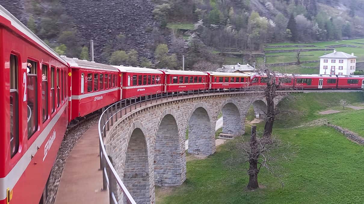 The red Bernina train curving across the stone spiral viaduct at Brusio