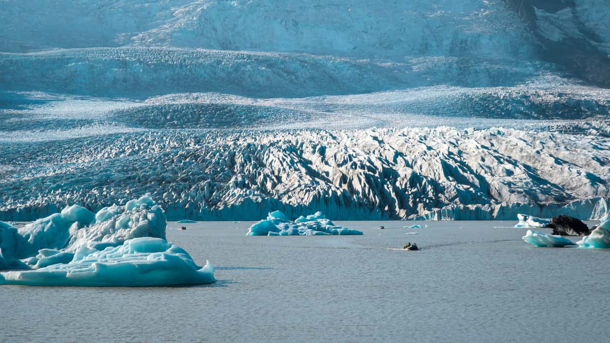 Icebergs drifting on Fjallsárlón lagoon below the crevassed front of Fjallsjökull glacier in Iceland