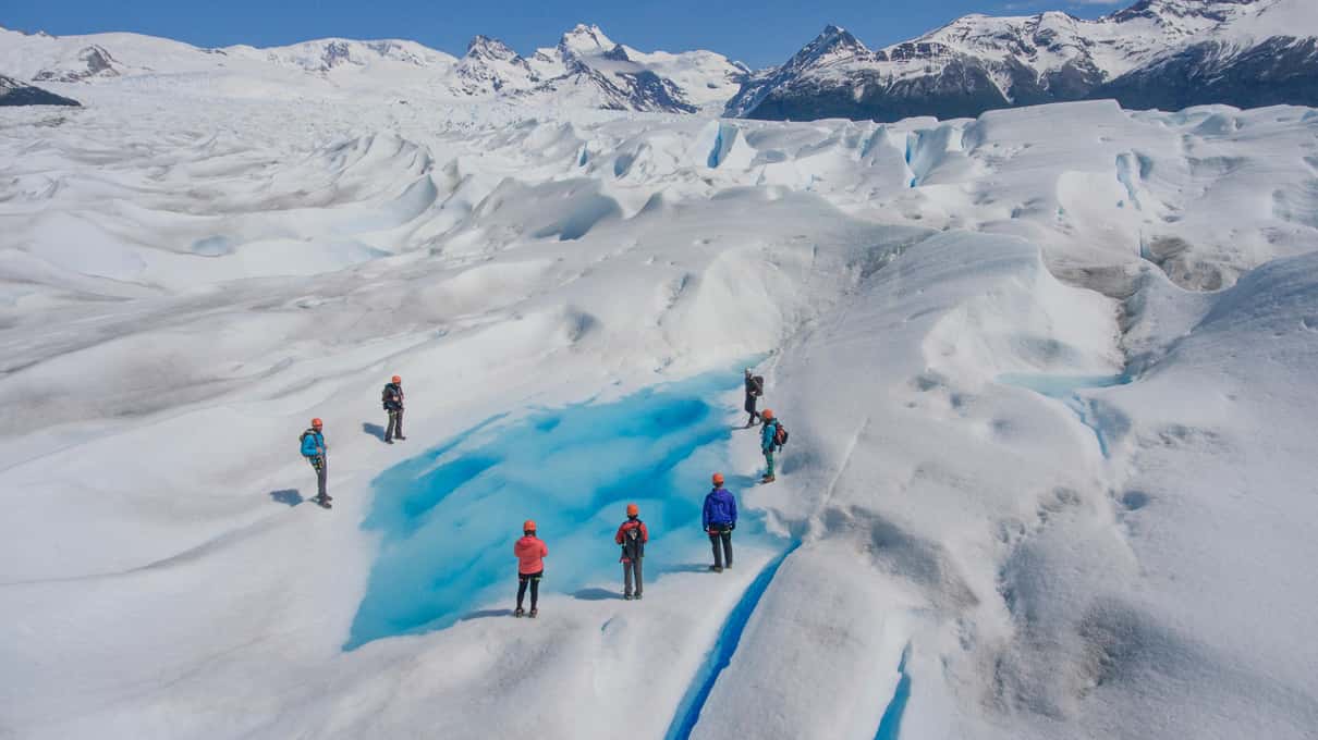 Big Ice hikers walking in single file across Perito Moreno Glacier past a bright blue lagoon