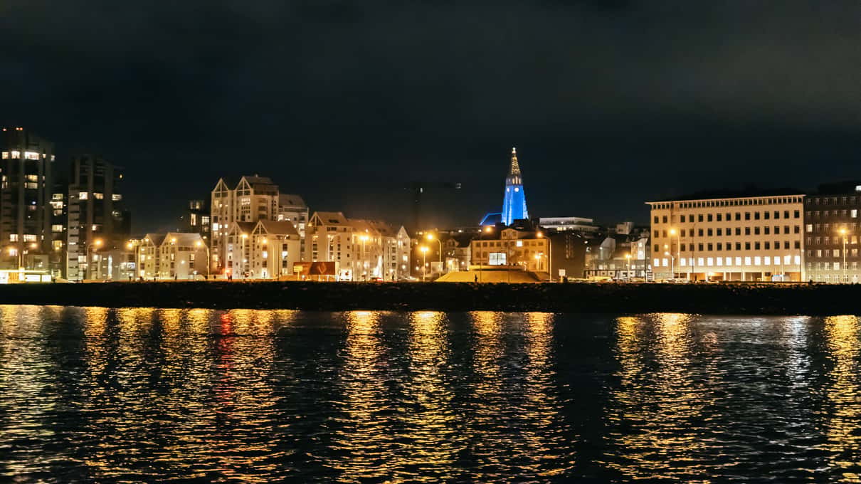 Reykjavik waterfront and the tower of Hallgrímskirkja lit up at night, seen from the water