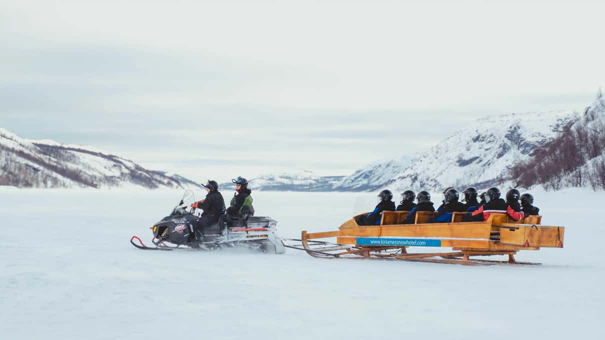 A snowmobile pulling a wooden passenger sled across the frozen fjord outside Kirkenes