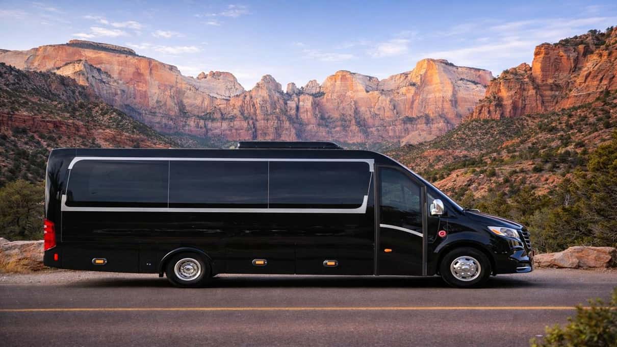 Ein schwarzer Mercedes-Sprinter-Van auf einer Straße unterhalb der roten Felswände des Zion Canyon in der Abenddämmerung